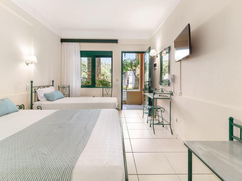 Jasný hotelový pokoj se dvěma postelemi a balkonem s výhledem.