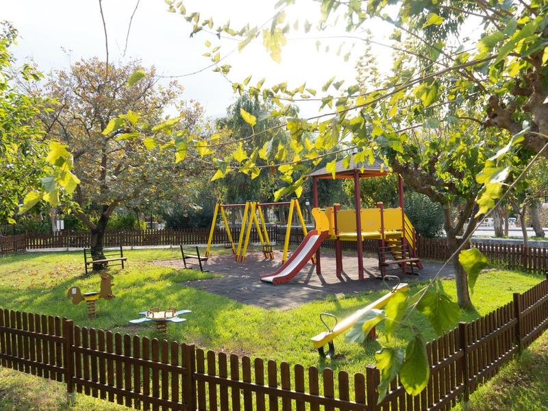 Dětské hřiště s klouzačkou a houpačkami, obklopené dřevěným plotem a stromy