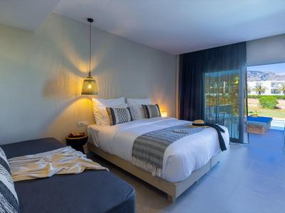 Habitación moderna con cama doble, sofá, lámpara colgante y vista a terraza con piscina.