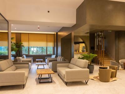 Moderna sala de hotel con sofás beige, mesas de centro y grandes ventanas con vista al verde.