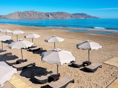 Playa de arena vacía con filas de tumbonas y sombrillas blancas cerca del mar tranquilo y montañas.