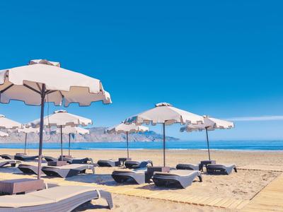 Leere Liegestühle mit Sonnenschirmen am Sandstrand unter klarem blauem Himmel