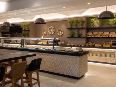 Estación de buffet moderna en hotel con iluminación, plantas y asientos en tonos cálidos.