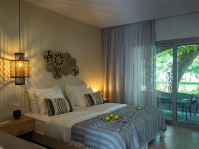 Habitación de hotel acogedora con cama doble, iluminación suave y acceso a un balcón con vista al verde.