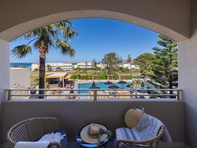 Balkon mit zwei Stühlen und Tisch mit Blick auf Palmen und Hotelanlage unter klarem Himmel.