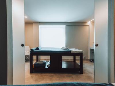 Sala de masajes con diseño moderno, cama de masaje centrada frente a ventana luminosa.