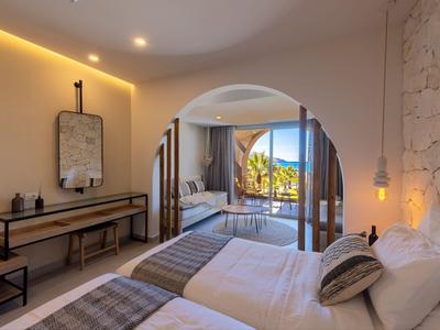 Helles Hotelzimmer mit zwei Betten, einem Spiegel und Terrasse mit Meerblick.