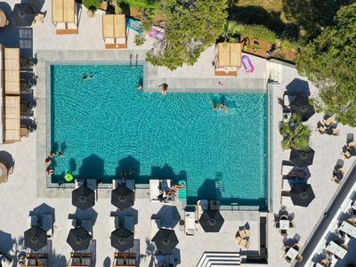 Oberansicht eines Schwimmbads mit Liegestühlen und Sonnenschirmen in einem Hotelgarten.