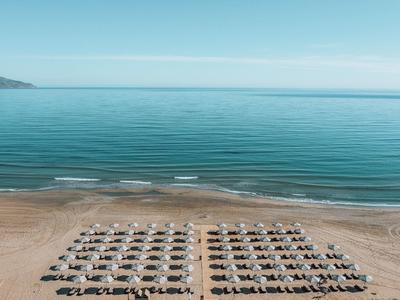 Strand mit Reihen von Sonnenschirmen und Liegestühlen vor ruhigem, blauem Meer, klarer Himmel.