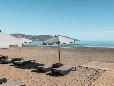 Leerer Sandstrand mit Liegen und weißen Sonnenschirmen unter klarem blauen Himmel.