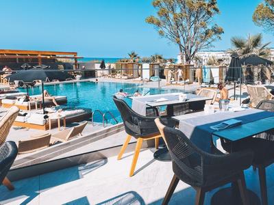 Moderner Außenbereich mit Pool, Tischen, Stühlen und Meerblick an einem sonnigen Tag.