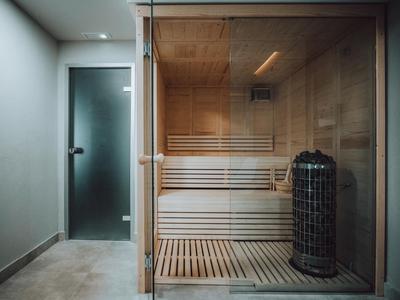 Sauna moderna con pared de vidrio, bancos de madera y horno eléctrico en un área de bienestar.