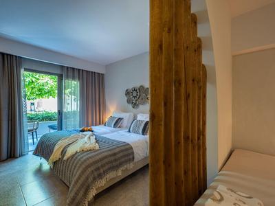 Gemütliches Schlafzimmer mit großem Bett, Holzwandteiler und Zugang zur Terrasse mit Garten.