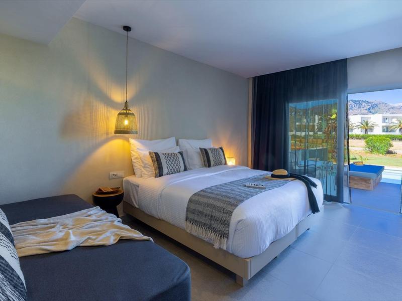 Habitación moderna con cama doble, sofá, lámpara colgante y vista a terraza con piscina.