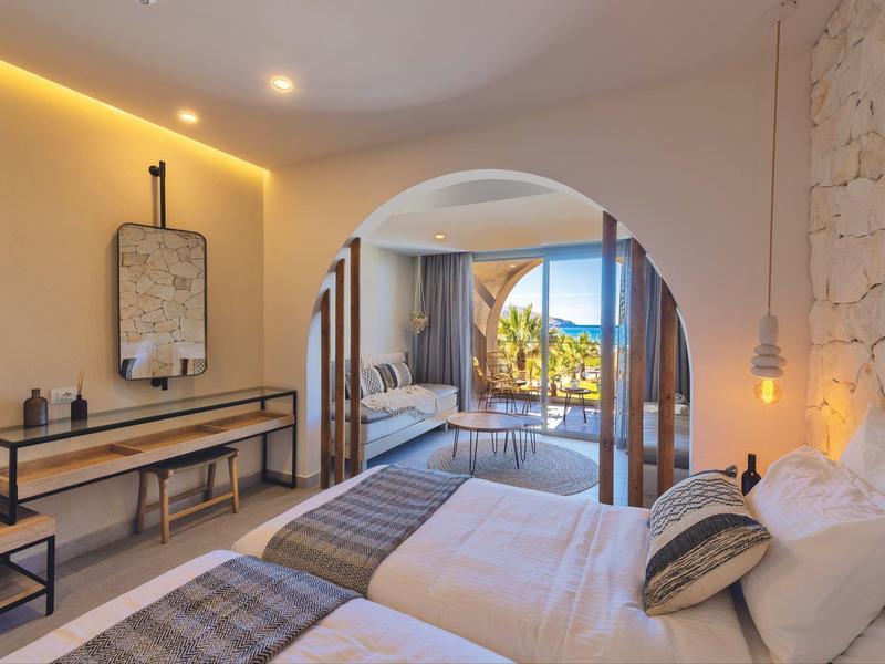 Habitación de hotel moderna con dos camas y vista a una terraza con jardín.