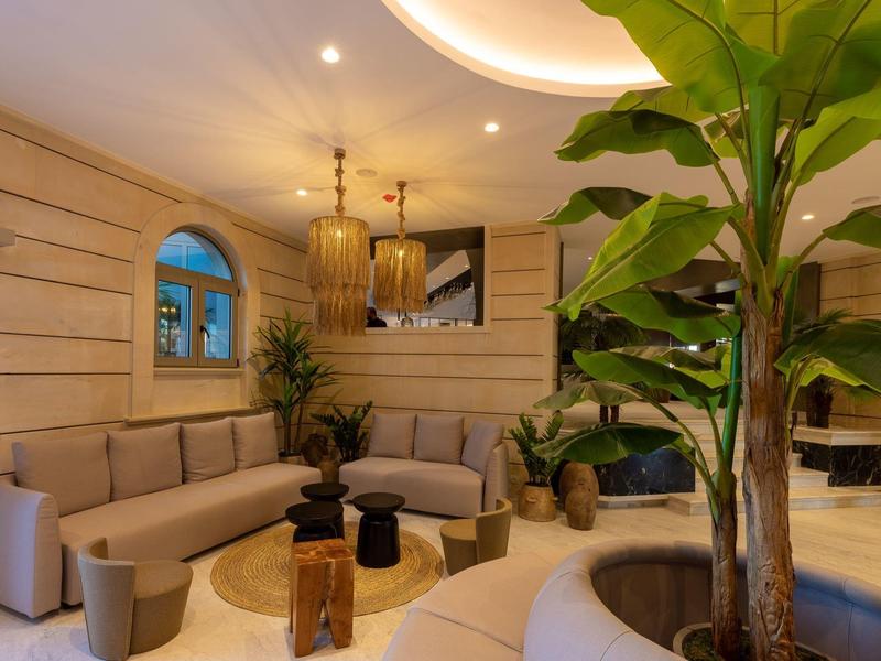 Sala moderna de hotel con paredes de madera, sofás, plantas y mesa de centro redonda bajo luz cálida.