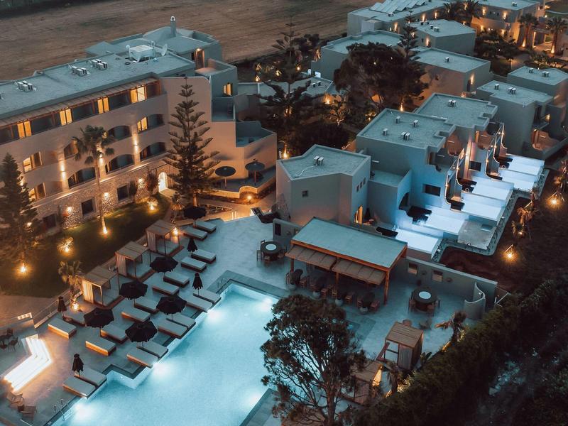 Vista de un hotel con piscina iluminada y tumbonas al atardecer.