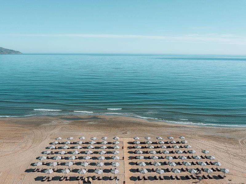 Playa con filas ordenadas de tumbonas y sombrillas frente a un mar azul tranquilo y cielo despejado.