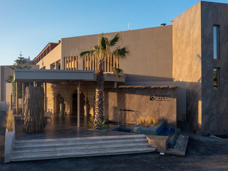 Edificio moderno de hotel con techo sombreado y palmeras al atardecer.