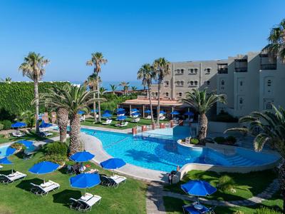 Hotelpool mit Liegestühlen, Palmen und umliegendem Garten unter blauem Himmel.