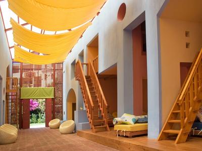 Innenhof eines Hotels mit gelben Sonnensegeln, Holztreppen und gemütlichen Sitzkissen.