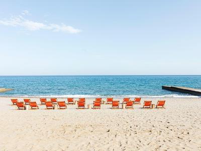 Leerer Sandstrand mit zwei Reihen oranger Liegestühle und klarem blauem Himmel.