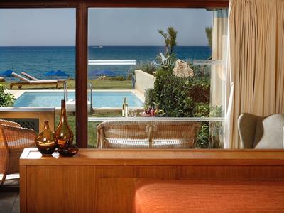 Blick durch ein Hotelzimmer auf einen Poolbereich und das Meer im Hintergrund.