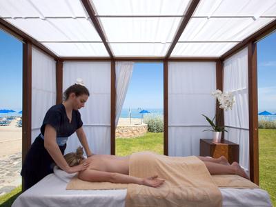 Masseurin gibt Massage in offenem Strandpavillon bei Sonnenschein.