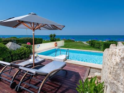 Zwembadgedeelte met ligstoelen en parasol met uitzicht op zee onder blauwe lucht