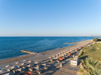 Strand mit Sonnenschirmen, Liegestühlen und Blick auf ruhiges Meer an einem klaren Tag