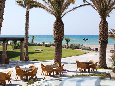 Blick auf eine Terrasse mit Tischen und Stühlen, Palmen und Meer im Hintergrund