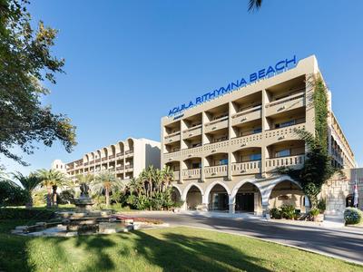 Hotel mit Balkonzimmern, Arkaden und großem Garten unter blauem Himmel.