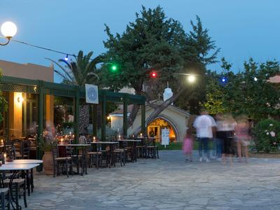 Abendliche Terrasse mit Tischen und Stühlen vor einem Restaurant, umgeben von Bäumen und Lampen.