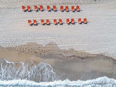 Sandstrand mit Reihen von orangenen Liegestühlen und welligem Meer im oberen Bereich.