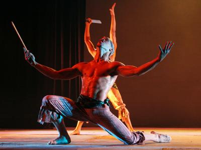 Zwei tänzerische Darsteller in dynamischer Pose auf einer beleuchteten Bühne.