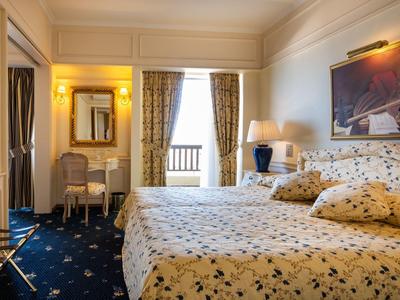 Elegantes Hotelzimmer mit Doppelbett, Schreibtisch, Vorhängen und beleuchteten Kunstwerken.