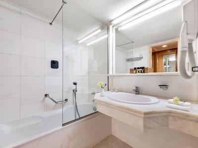 Baño moderno de hotel con bañera blanca, lavabo y espejo grande.