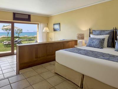 Habitación de hotel luminosa con cama grande, vista a la terraza y al mar al fondo.