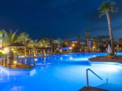 Piscina del hotel iluminada con palmeras y lounges por la noche bajo cielo despejado.