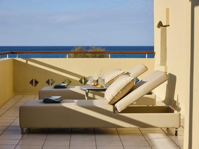 Dos cómodas tumbonas en una terraza soleada de hotel con vista al mar.