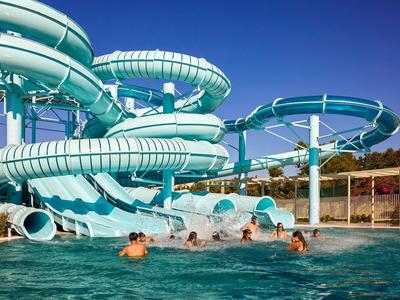 Toboganes de agua azules retorcidos sobre una piscina con personas jugando debajo.