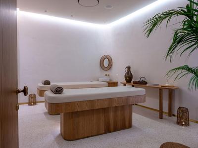 Habitación de spa luminosa con camilla de masaje, decoración minimalista y planta verde en la esquina.