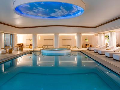 Piscina cubierta moderna con área de spa y tumbonas en un hotel de lujo.