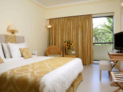 Gemütliches Hotelzimmer mit Doppelbett, goldener Bettdecke und Balkon mit Pflanzenblick.