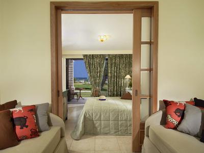 Blick in Schlafzimmer mit hellen Wänden, grünen Vorhängen und beige Sofa mit bunten Kissen.