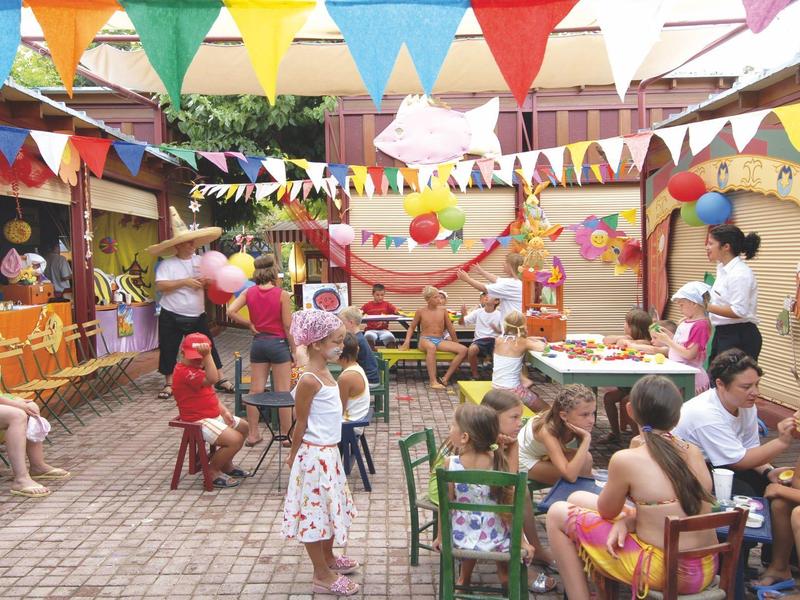 Kinder feiern eine bunte Party mit Girlanden und Luftballons in einem Innenhof.