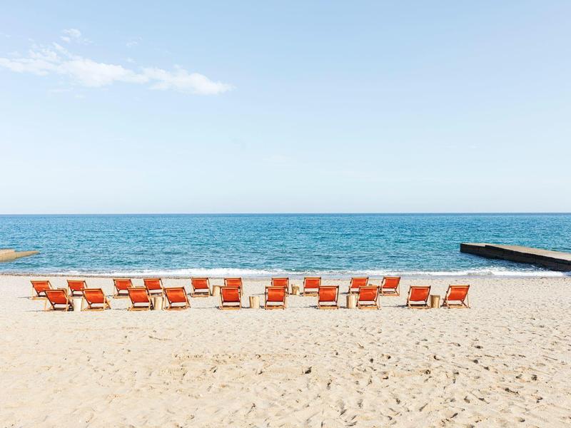 Leerer Sandstrand mit zwei Reihen oranger Liegestühle und klarem blauem Himmel.
