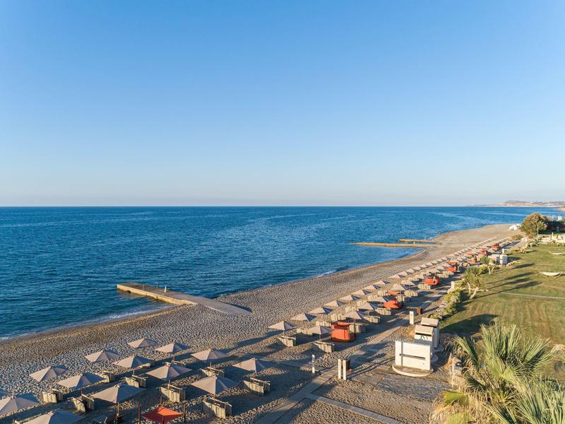 Strand mit Sonnenschirmen, Liegestühlen und Blick auf ruhiges Meer an einem klaren Tag