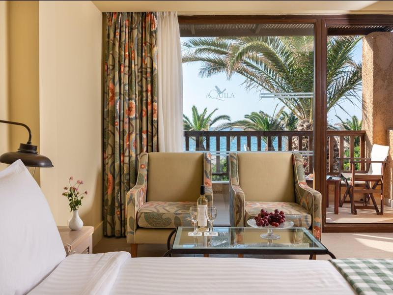 Gemütliches Hotelzimmer mit Sitzbereich, Balkon und Blick auf Palmen