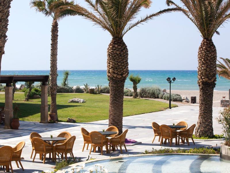 Blick auf einen Außenbereich mit Palmengarten und Sitzgruppen vor dem Meer.